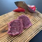 Twee steak tartaar op een houten snijplank, met een groot mes en een rode paprika op de achtergrond.